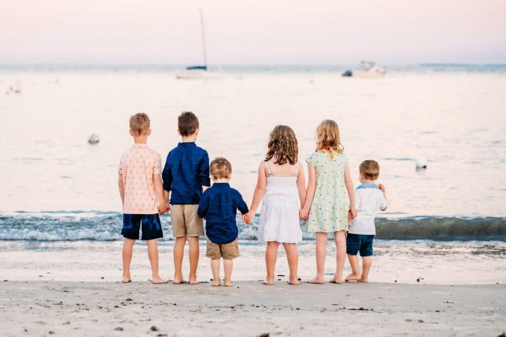 Little kids holding hands looking out at water at golden hour at the beach in NH.