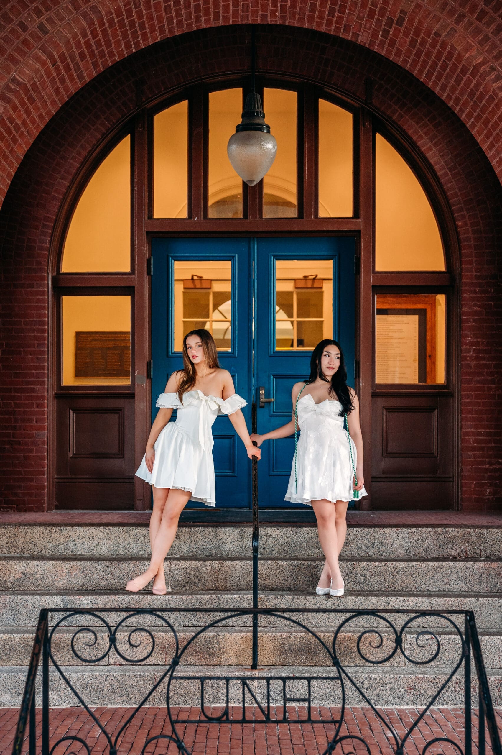 College grad photographer capturing two University of New Hampshire graduates posing together in front of campus doors for senior portraits.