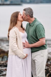 Expectant couple kissing at Newcastle Commons beach during their maternity session.