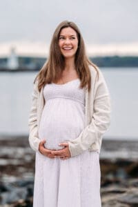 Mom to be laughing and cradling belly at maternity photo session in Newcastle, NH