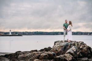 Expectant couple standing on rocks at Newcastle Commons beach during their maternity session.