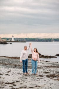 Expectant couple dancing on rocks at Newcastle Commons beach during their maternity session.
