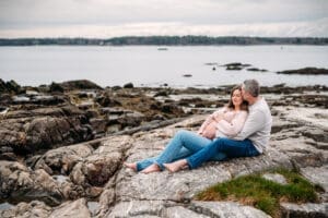 Expectant couple sitting on rocks at Newcastle Commons beach during their maternity session.