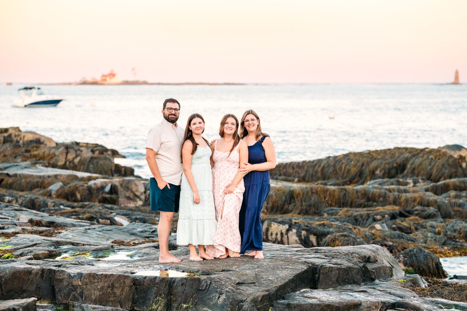Family with teenage daughters standing on rocks at their summer mini session in NH.